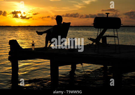 Ein Reisender genießt eine Sunset Grill auf einem Steg auf der schönen Tabak Caye, Belize, sunset BBQ Stockfoto