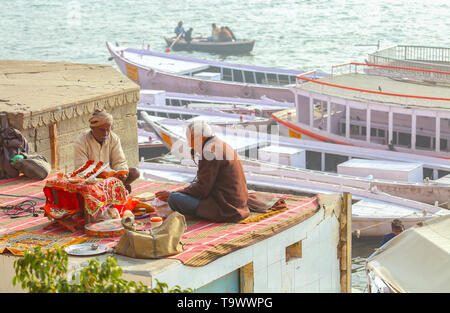 Im Alter von hinduistischen Mann mit Priester singt religiöse Hymnen an die Varanasi Ganges ghat mit Blick auf touristische Boot auf dem Fluss Ganges Stockfoto