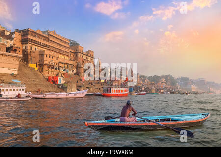 Historische Varanasi Stadt Architektur bei Sonnenuntergang mit Blick auf einen bootsmann Rudern auf dem Fluss Ganges Stockfoto