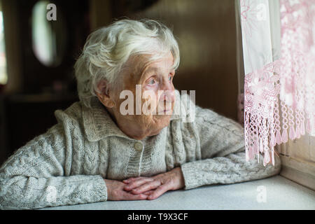 Eine ältere Frau sieht traurig aus dem Fenster. Pflege für einsame Rentner. Stockfoto