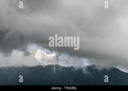 Bali, Indonesien - 25. Februar 2019: Regnerischen cloudscape über dunklen bewaldeten Berge in Bedougoel. Schattierungen von Grau. Stockfoto