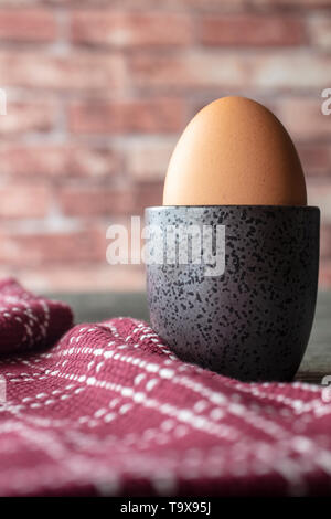 Weich gekochtes Ei in eine Tasse mit einem Geschirrtuch auf rustikalem Tisch und Backstein Hintergrund Stockfoto