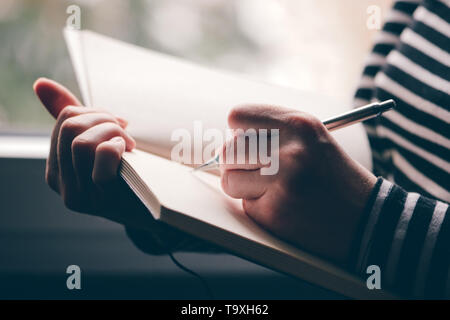 Linkshändige Frau schreiben Tagebuch, in der Nähe der Hände mit Bleistift und Notizbuch Stockfoto