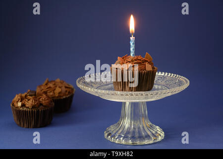 Schokolade Kuchen mit einer brennenden Kerze auf einem Glasgefäß, zwei weitere auf der einen Seite, tief blauen Hintergrund mit Kopie Raum, ausgewählte konzentrieren, schmale tiefe der f Stockfoto