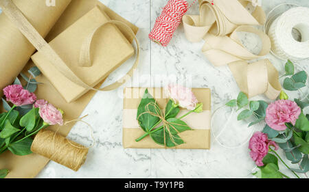 Null - Abfall Geschenkverpackung flatlay Overhead mit Kraftpapier, Jute und Baumwolle Bänder und Garten Blumen für umweltfreundlichen Lebensstil. Stockfoto