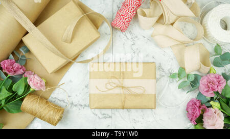 Null - Abfall Geschenkverpackung flatlay Overhead mit Kraftpapier, Jute und Baumwolle Bänder und Garten Blumen für umweltfreundlichen Lebensstil. Stockfoto