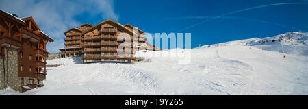 Panorama der schneebedeckten Piste in einem alpinen Skigebiet mit Apartment Gebäude am Hang Stockfoto