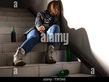 Bewusstlose junge Frau mit leeren Flaschen sitzen auf der Treppe. Konzept des Alkoholismus Stockfoto