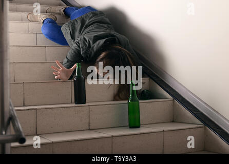 Bewusstlose junge Frau mit leeren Flaschen liegend auf Treppen. Konzept des Alkoholismus Stockfoto