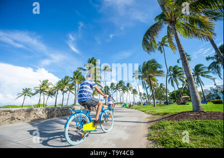 Touristen fahren Fahrräder entlang der Strandpromenade in Lummus Park neben historischen Ocean Drive in South Beach, Miami, Florida, USA Stockfoto