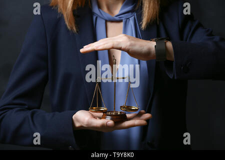 Weibliche Rechtsanwalt holding Waage der Gerechtigkeit auf dunklem Hintergrund, Nahaufnahme Stockfoto