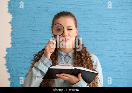 Junge Frau mit schlechten Augen holding Buch und Lupe auf farbigen Hintergrund Stockfoto