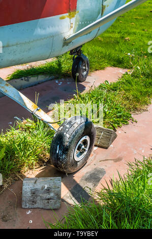 Alten kleinen einmotorigen Flugzeug Rad und Holzkeile auf Parkplatz pad, splattered mit Schmutz und Vogel Ausscheidungen. Stockfoto