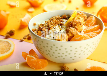 Lecker Müsli mit Joghurt und Obst in Schüssel auf farbigen Hintergrund Stockfoto