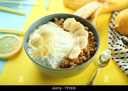 Lecker Müsli mit Joghurt und Obst in Schüssel auf farbigen Hintergrund Stockfoto