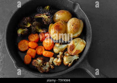 Gebratenes gebratenes Gemüse in einer gusseisernen Pfanne mit Kartoffeln, Blumenkohl, Karotten und Brokkoli. Auf einer schiefertafel Hintergrund. Stockfoto