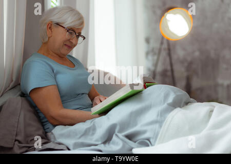 Charmante Dame im Bett liegt und sich im Buch zu lesen. Stockfoto