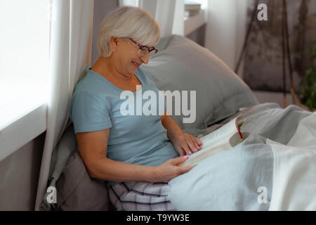 Lächelnd strahlende Dame gerne ein Buch lesen im Bett. Stockfoto