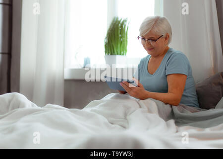 Lächelnd weibliche Klick auf die Tablette während im Bett lag, Stockfoto