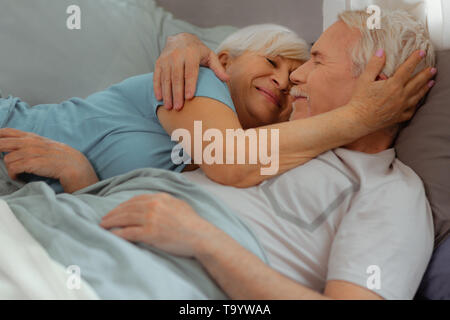 Liebevolle Frau zärtlich umarmte ihre Ehepartner beim Lügen mit ihm Stockfoto