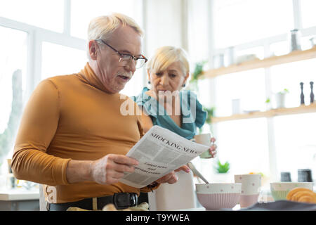 Konzentriert gekleideter stattlicher Silberhaarige männlichen Engagieren in einer Zeitung lesen Stockfoto