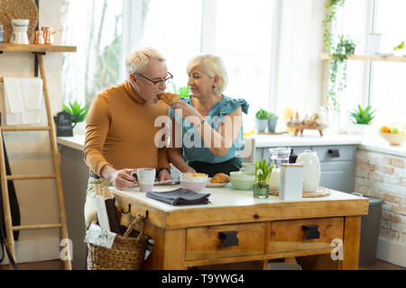 Glühende Frau zärtlich auf die Fütterung der alte Ehegatte mit Croissant Stockfoto