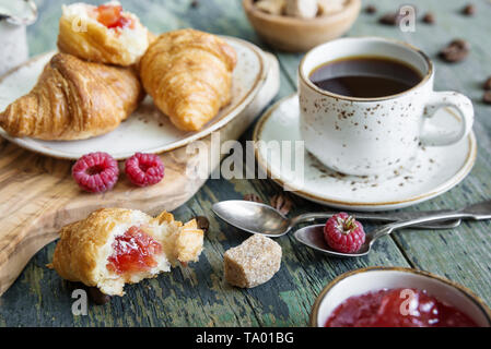 Ein leichtes Frühstück, bestehend aus einer Tasse schwarzen Kaffee und Croissants mit einer Füllung aus himbeermarmelade Stockfoto