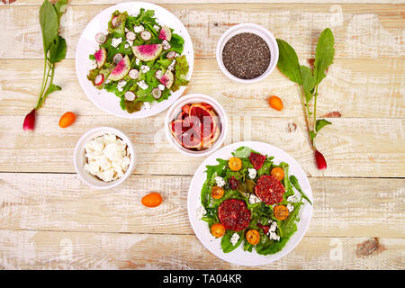 Mix Salate auf Holz- Hintergrund. Frischem Zitrus Salat mit Rucola Feta, Chia, kumquat und Blut orange. Wassermelone Rettich Salat. Vegan, Vegetarisch, c Stockfoto