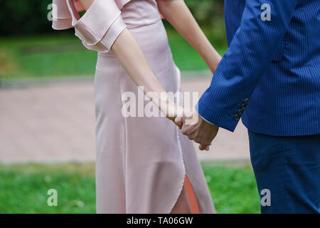 Kaukasische Paar, Braut in Ivory satin kleid und der Bräutigam im dunkelblauen Anzug, Hände halten, mit einem unscharfen, out-of-focus Hintergrund Stockfoto