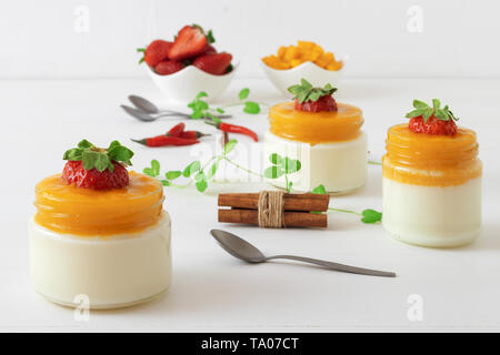 Traditionelle italienische süßes Dessert Panna cotta mit Mango Gelee mit Hauch von red hot chili Piri-Piri in Töpfen auf weissem Holztisch und embellis serviert. Stockfoto