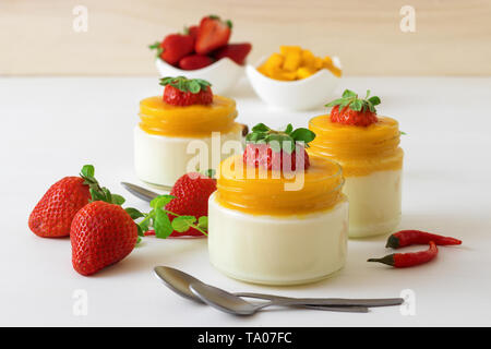 Traditionelle italienische süßes Dessert Panna cotta mit Mango Gelee mit Hauch von red hot chili Piri-Piri in Töpfen auf weissem Holztisch und embellis serviert. Stockfoto