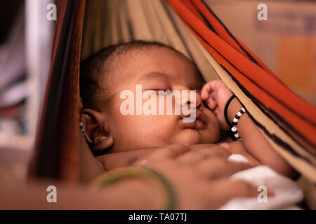 Nahaufnahme von niedlichen kleinen New Born Baby schlafen in der Wiege aus Saree mit Müttern hand auf Baby Stockfoto