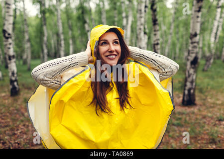 Glückliche junge Frau im gelben Regenmantel Wandern im Frühjahr Wald unter Regen und Spaß haben. Das Leben genießen Stockfoto
