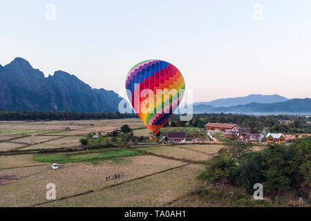 Gestreifte Heißluftballons über der Erde fliegen, abendliche Landschaft und Stadt mit kleinen Häusern, in Laos, Vang Vieng. Laos. Stockfoto