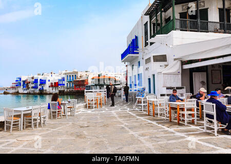 Mykonos, Griechenland - 23. April 2019: Leute, Promenade mit Stühlen und Tischen im typisch griechischen Taverne in Klein Venedig Teil der Stadt Mykonos, Stockfoto