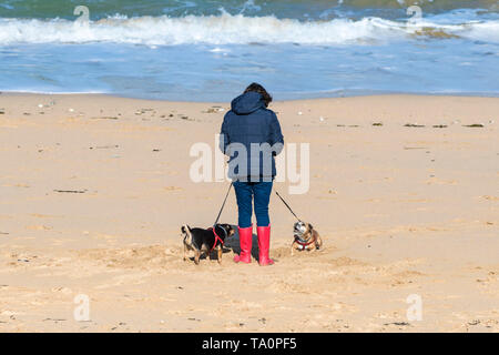 Eine Frau das Tragen der roten Gummistiefel und gehen mit ihrem Hund auf den Fistral Beach in Newquay in Cornwall. Stockfoto