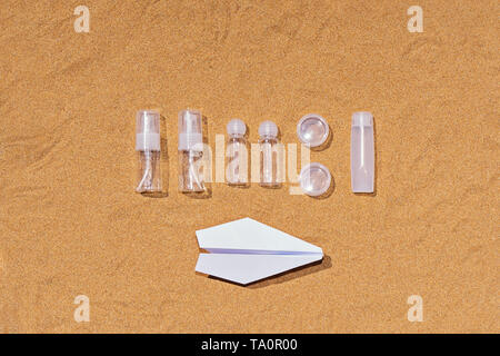 Blick von oben auf die kosmetische Kunststoffbehälter für Reisen im Flugzeug auf sandigem Hintergrund Stockfoto