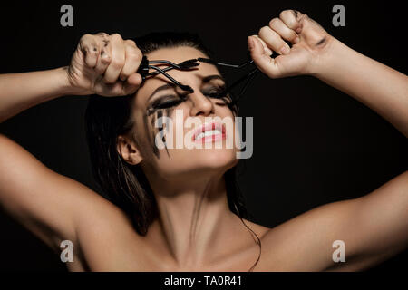 Schöne Frau mit Flecken von Make-up im Gesicht und gebrochen mascara Bürsten in ihren Händen Stockfoto