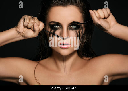 Schöne Frau mit Flecken von Make-up im Gesicht und gebrochen mascara Bürsten in ihren Händen Stockfoto