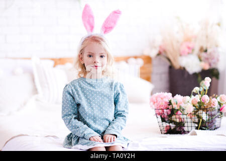 Cute Baby Mädchen 4-5 Jahre alte stilvolle Kleidung tragen und Rabbit Ears Stirnband mit Blumen im Hintergrund. Mit Blick auf die Kamera. Frühling. Stockfoto