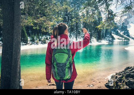 Schöne junge Frau mit Rucksack, eine selfie am See an einem sonnigen Tag im Frühling. Landschaft mit sportliche Mädchen im roten Mantel, Foto, gree Stockfoto