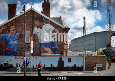 Ein Mann hinter einem Wandbild von Künstler Paul Curtis auf die giebelseite eines Hauses in Prenton, Wirral mit zwei Tranmere Rovers Spieler. Das Wandbild ist nur außerhalb des Stadion des Clubs, Prenton Park entfernt. Tranmere Rovers gewonnen Förderung zu EFL League 2 aus der Nationalen Liga über einen Play-off in der Saison 2017-8 und kehrte 12 Monate später, am 25. Mai zum Wembley Newport County für einen Platz in der EFL-Liga eine zu Gesicht. Stockfoto