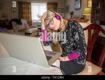 Eine Mutter zu Hause, mit Ihrem Computer angezeigte Mischung aus Unterhaltung und Traurigkeit online an, was sie sieht. Stockfoto