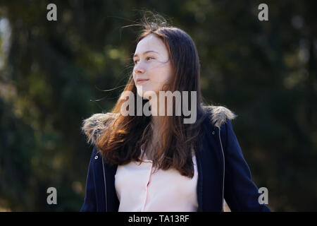 Ein schönes Mädchen in einen blauen Mantel mit Losen rötliche Haare, die im Wind, steht vor dem Hintergrund des Waldes. Stockfoto