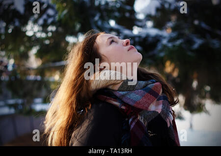 Ein schönes Mädchen in warme Kleidung und mit langen rötliche Haare steht in der Mitte der Winter Forest und schaut nach oben, bis der Schnee auf sie fällt. Stockfoto