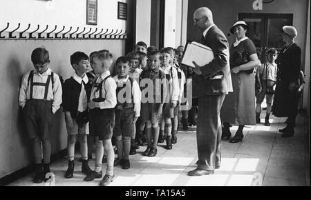 Schüler nach Ihrer ersten Lektion vor dem Klassenzimmer mit ihrem Lehrer. Im Hintergrund sind wahrscheinlich zwei Mütter, die ihre Kinder abholen. Stockfoto