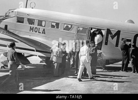 Foto eines deutschen Junkers Ju 52 der spanischen Fluggesellschaft Iberia 1939 am Flughafen von Salamanca, Kastilien und Leon, Spanien, durch die Fenster des neuen Terminals. Soldaten und Zivilisten sind, wenn Sie aus dem Flugzeug. Die Maschine ist 'Mola' benannt, nach General Emilio Mola Vidal (gestorben 1937), einer der Führer des Aufstandes von General Francisco Franco. Während des Bürgerkriegs, die Deutsche Lufthansa und die Iberia (gegründet 1927) durchgeführten Flüge meist mit deutschen Piloten in den Spanischen Nationalen Zone ab 1937 geplant. Die Flugzeuge wurden von der Deutschen Lufthansa AG zur Verfügung gestellt. Stockfoto