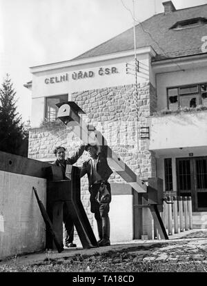 Zwei bewaffnete Männer öffnen Sie die tollgate Grenzübergang an der Grenze German-Czechoslovak in Bayern bei Waidhaus am 28. September 1938. Ein Gewehr ist lehnte sich gegen die Wand auf der linken Seite. Im Hintergrund, die geräumt customhouse. Stockfoto