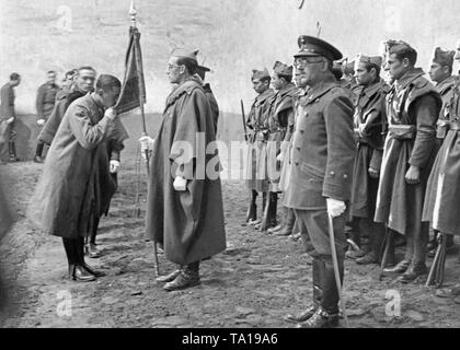 Das Foto zeigt ein Offizier in Uniform und loden Cape, wie er küsst das Bandera (die rot-gelb-roten Flagge Spaniens, die von einer grösseren gehalten) während seiner Vereidigung. Zuvor gab es einen Gottesdienst in der Burgos Officer Candidate School in Kastilien und Leon, Spanien. In den vorderen, einem Dozenten und einem Leutnant mit einem Säbel und ein Regenschirm. Stockfoto