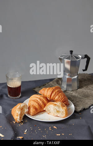 Glas von aromatischen Kaffee und Teller mit frisch gebackenen Croissants auf grauem Hintergrund. Kontinentales Frühstück Konzept. Für Text platzieren. Stockfoto